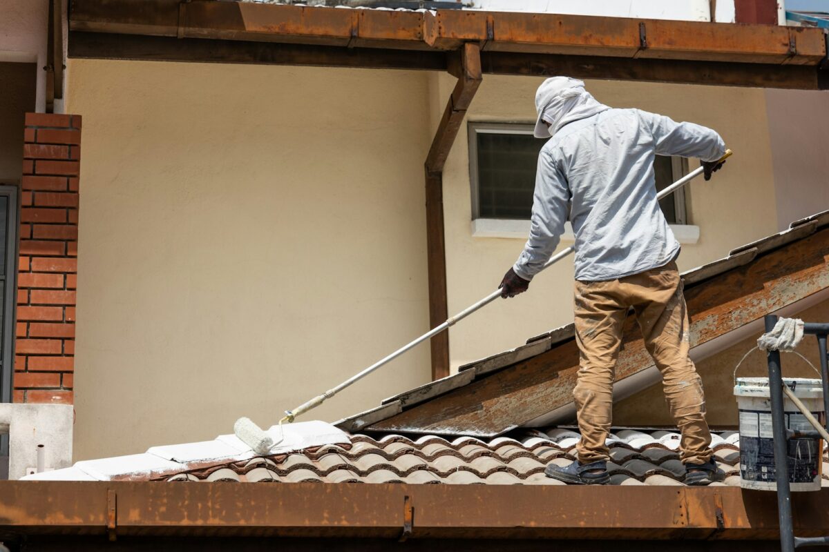 Worker adding undercoat foundation paint onto rooftop with roller at residential building in