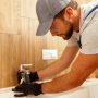 Serious plumber, male worker in uniform installing tap or bathroom faucet